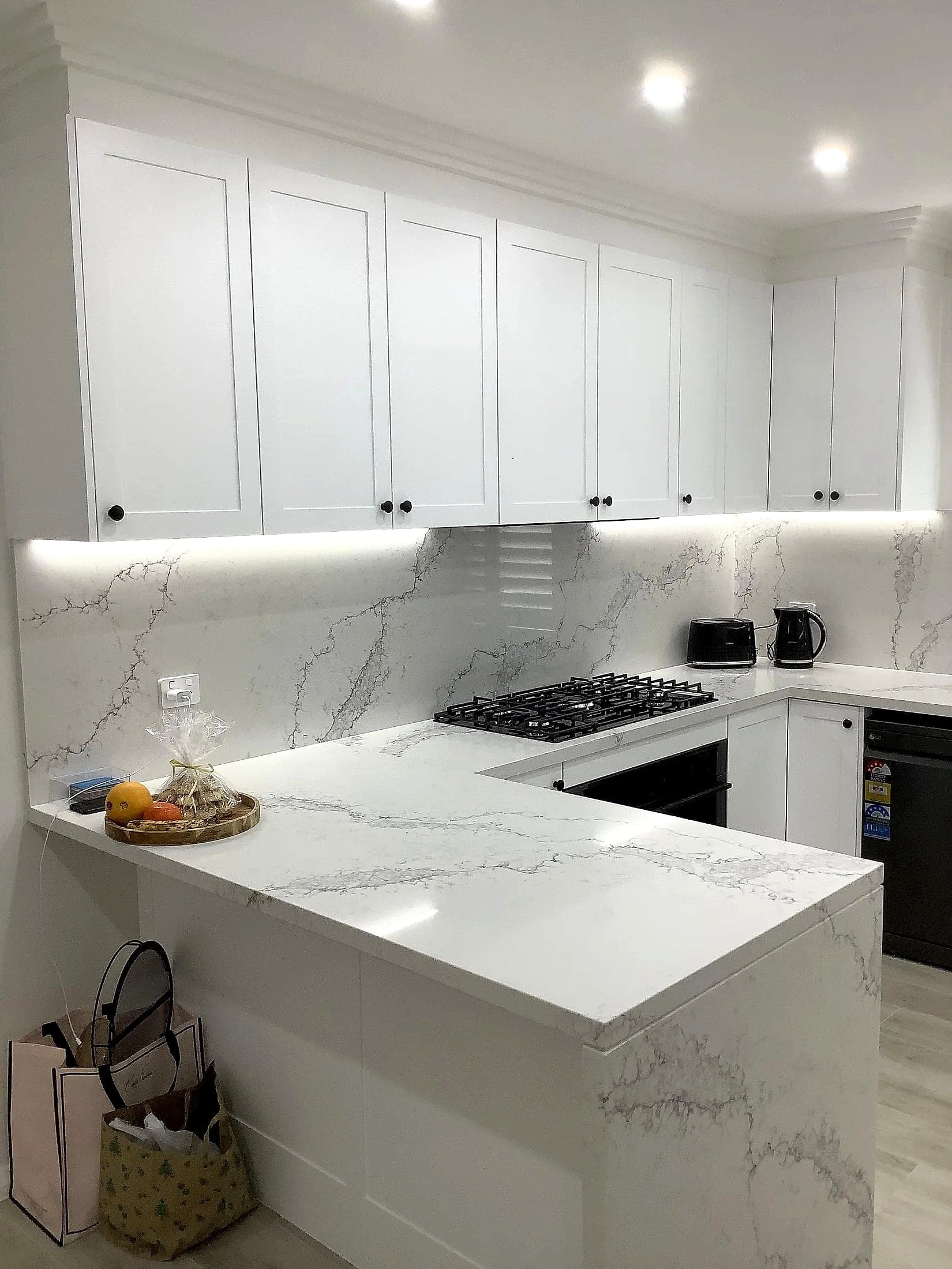 Marble-look splashback with LED strip lighting above a gas cooktop, by H&R Kitchens