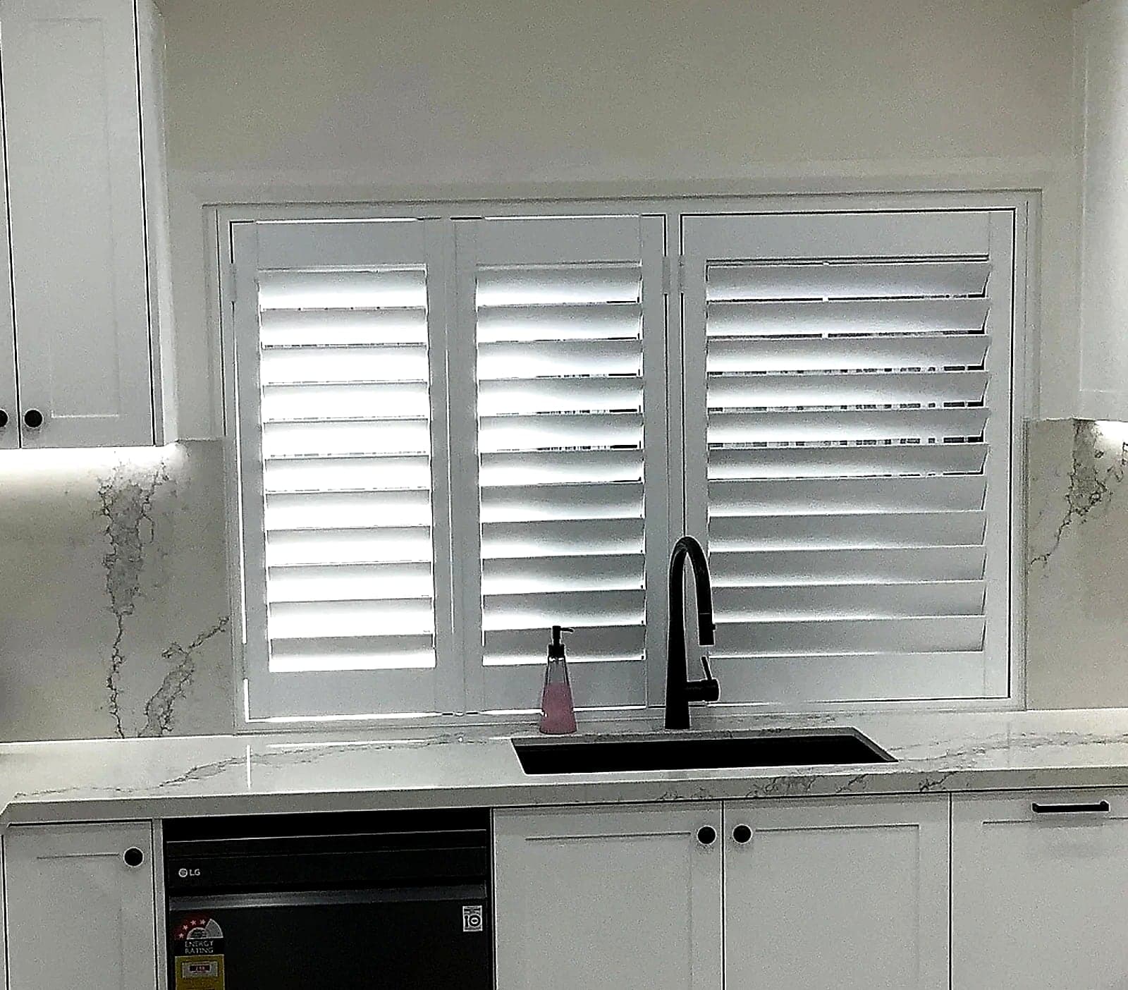 White shaker kitchen cabinetry with marble-look surfaces and black hardware by H&R Kitchens