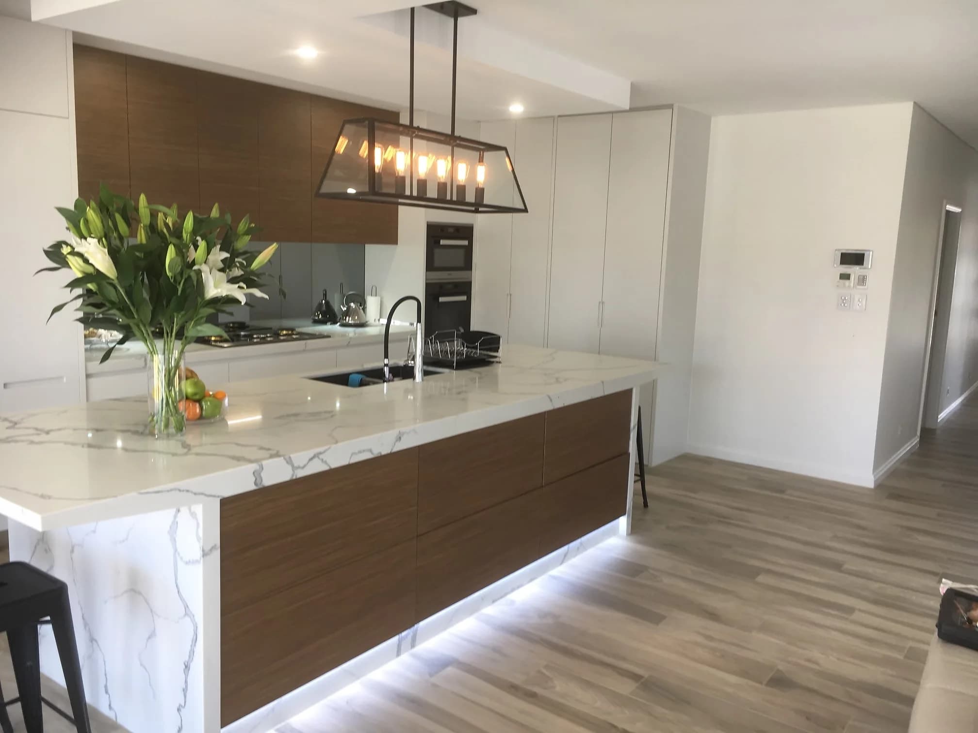 Warm two-tone kitchen with timber and white cabinetry, a marble-look waterfall island and a feature ceiling, by H&R Kitchens