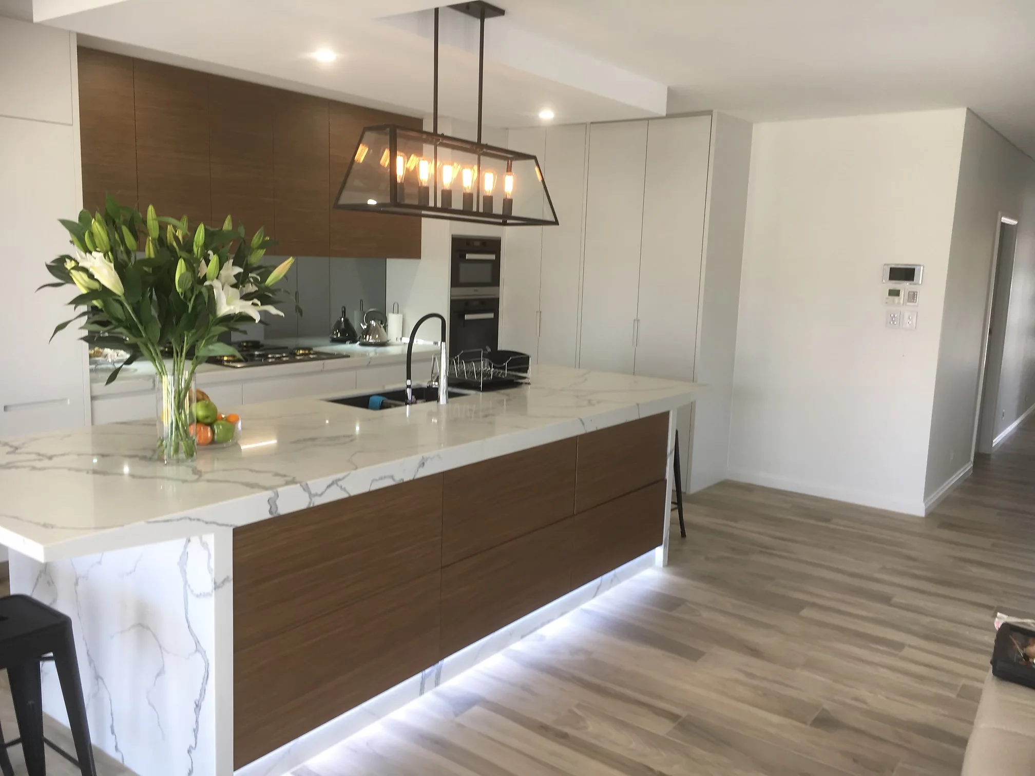 Warm two-tone kitchen with timber and white cabinetry, a marble-look waterfall island and a feature ceiling, by H&R Kitchens