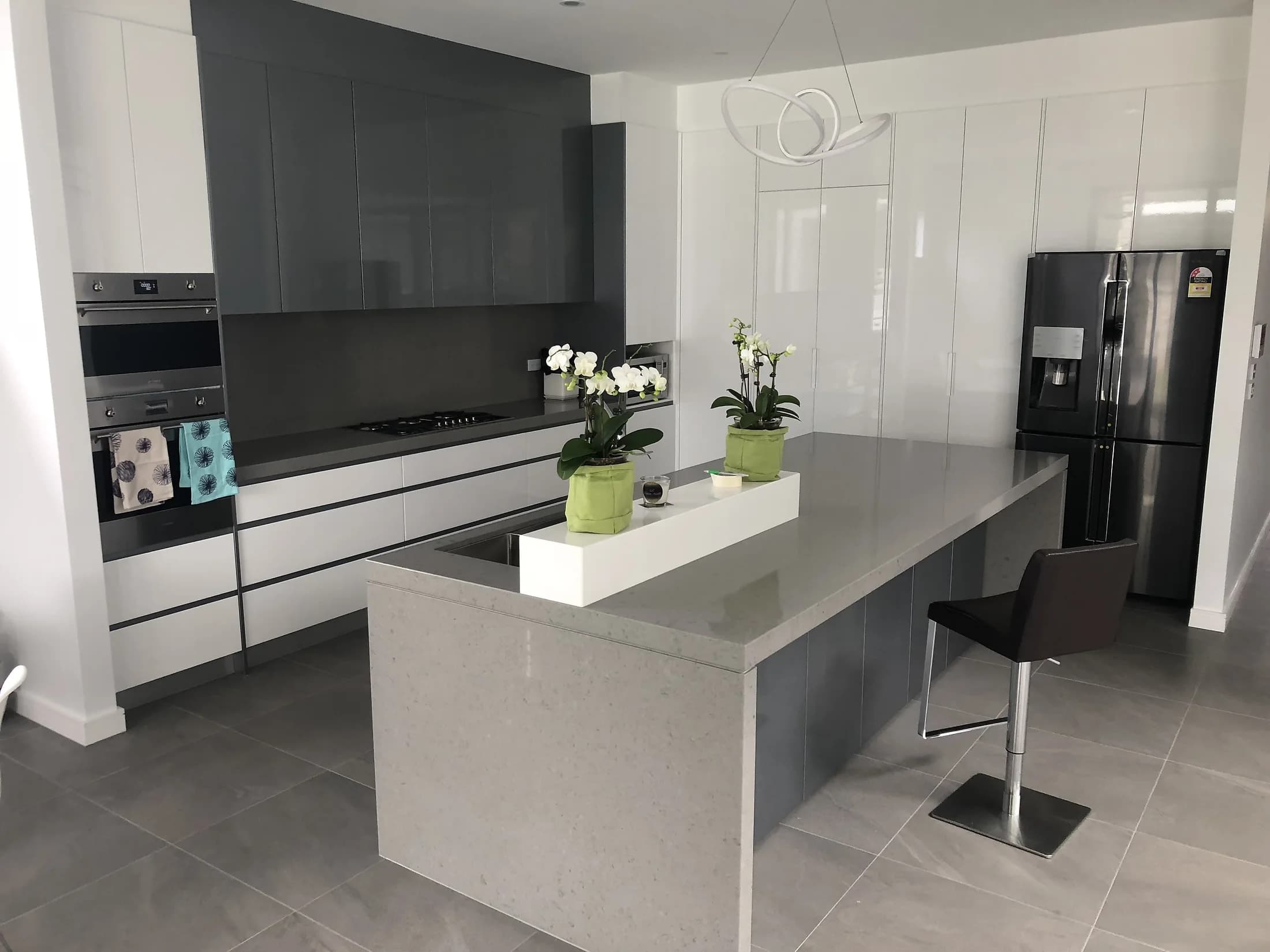Grey and white handleless kitchen with a waterfall island and sculptural ring pendant by H&R Kitchens