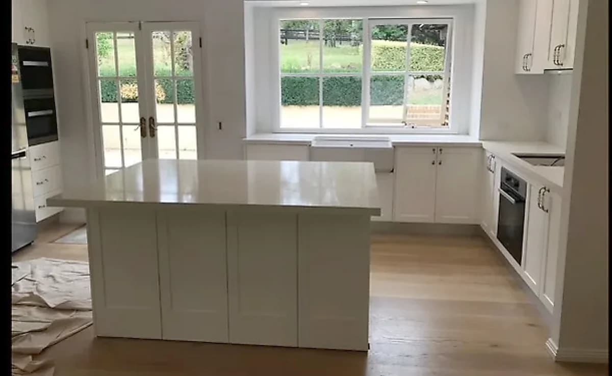 Classic white shaker kitchen with a central island, farmhouse-style sink and French doors by H&R Kitchens