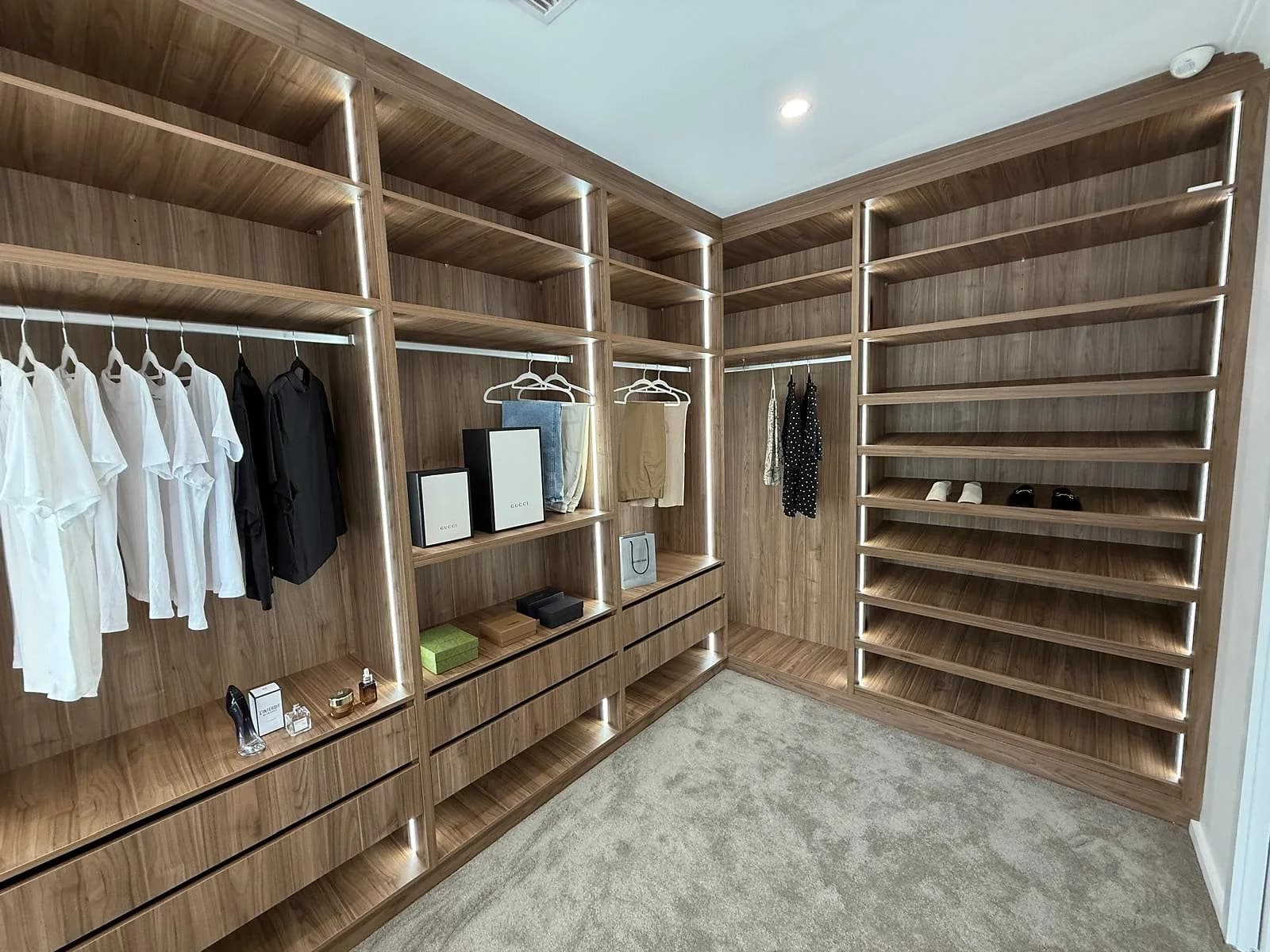 Walk-in wardrobe storage with timber shelving, drawers and integrated lighting by H&R Kitchens