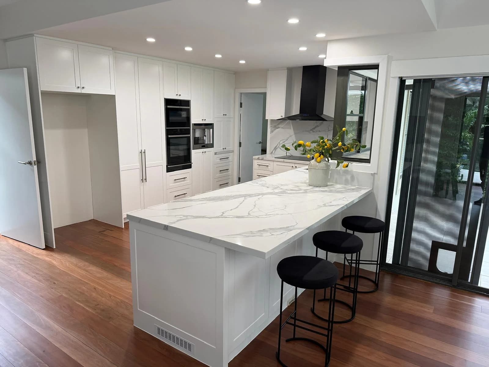 White shaker kitchen with black-framed openings, marble-look surfaces and a long peninsula by H&R Kitchens