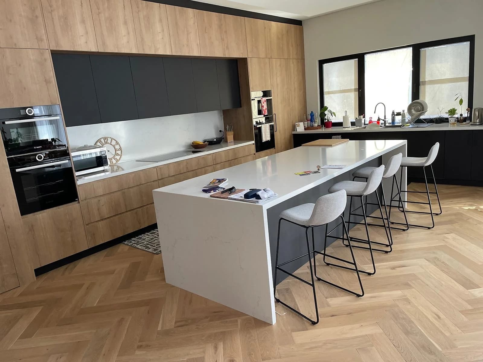 Open-plan kitchen with timber cabinetry, black overhead cabinets, integrated appliances and island storage, by H&R Kitchens