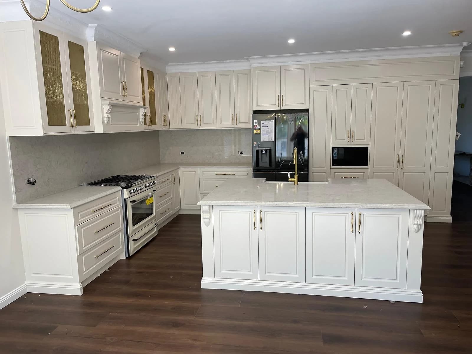 Completed white kitchen with a central island, tall storage and timber flooring by H&R Kitchens
