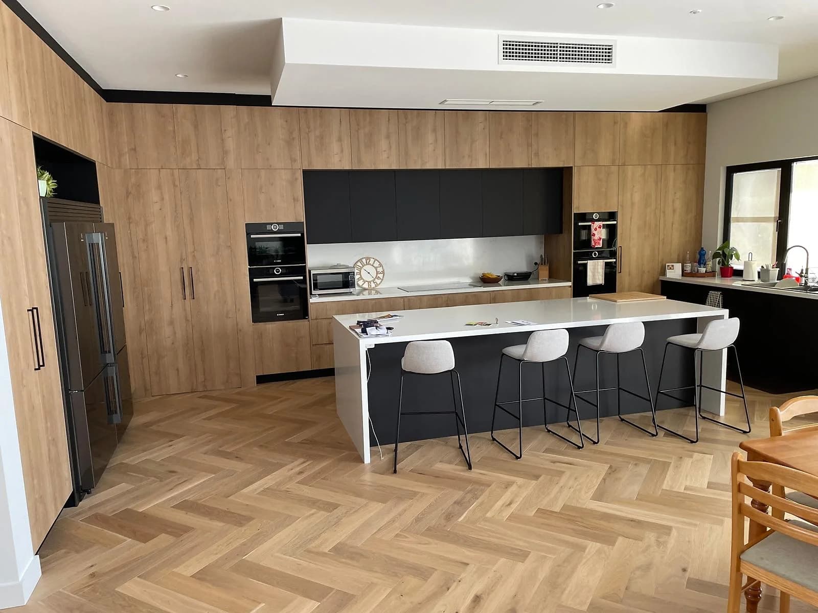 Timber and black kitchen with a long island, integrated appliances and herringbone flooring, designed by H&R Kitchens