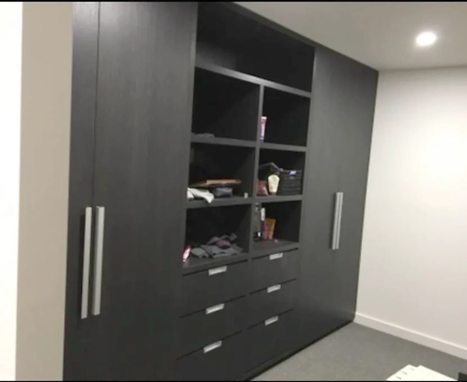 Dark grey fitted bedroom wardrobes with long handles, open cubbies and drawer storage by H&R Kitchens