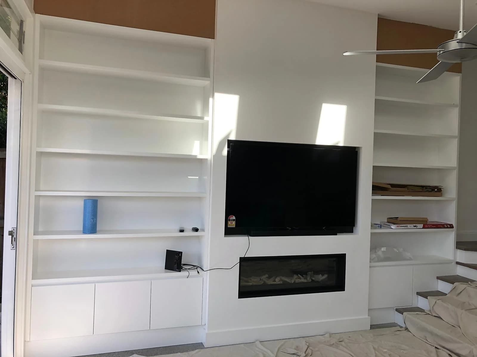 White living-room media wall with landscape fireplace, open shelves and stair-side joinery by H&R Kitchens