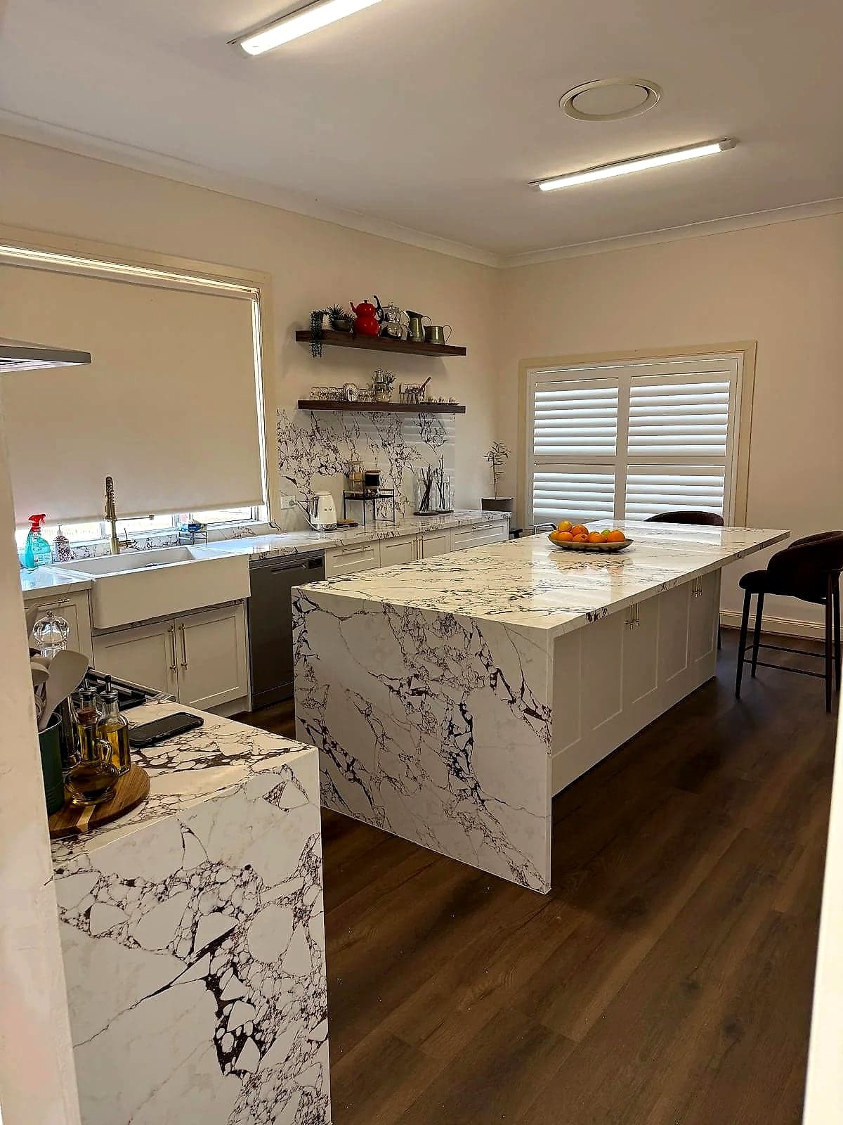 Kitchen with bold marble-look waterfall benchtops and timber flooring by H&R Kitchens