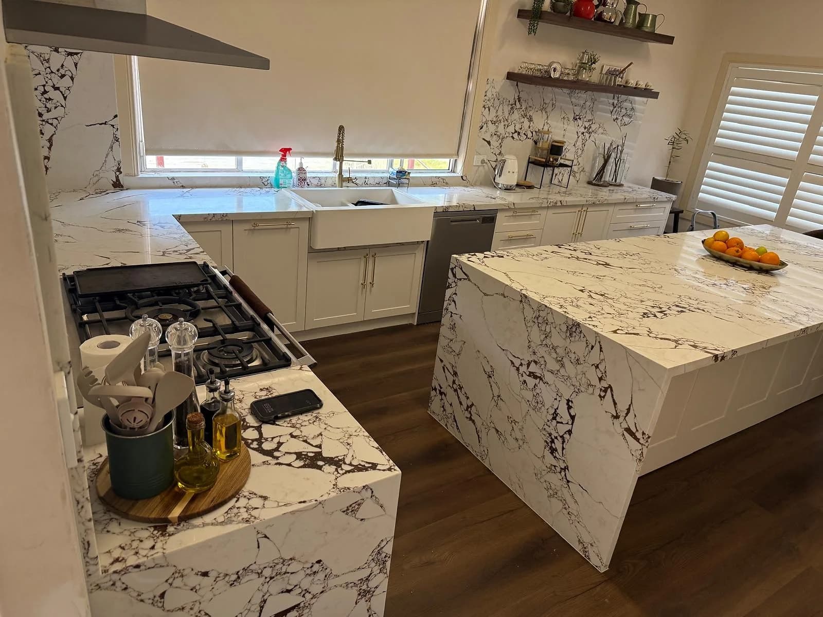 White shaker kitchen with gold hardware, strongly veined marble-look surfaces and a large island by H&R Kitchens