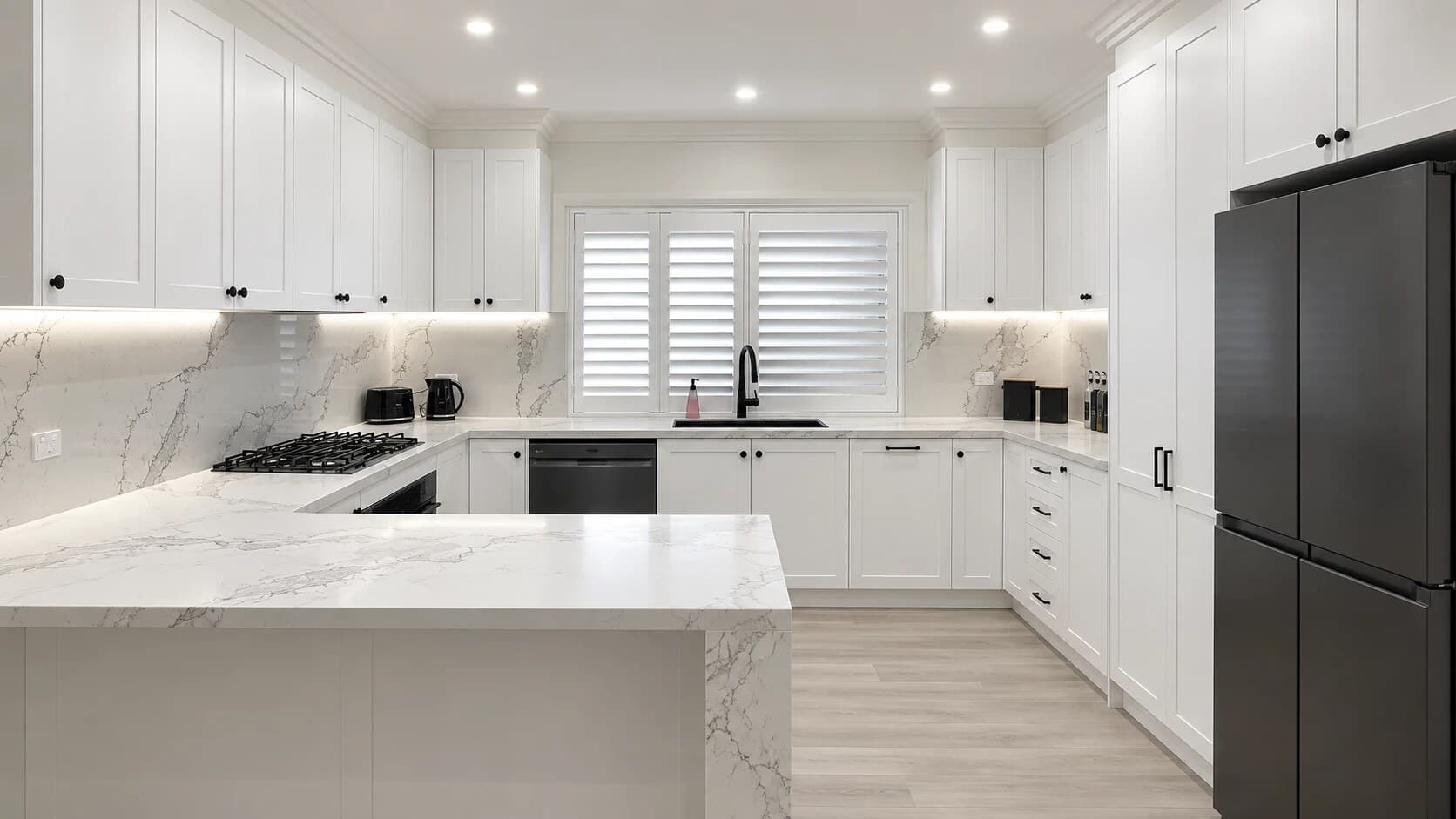 Guildford kitchen with white shaker cabinetry, a marble-look waterfall peninsula and full-height splashback, plantation shutters and a black fridge