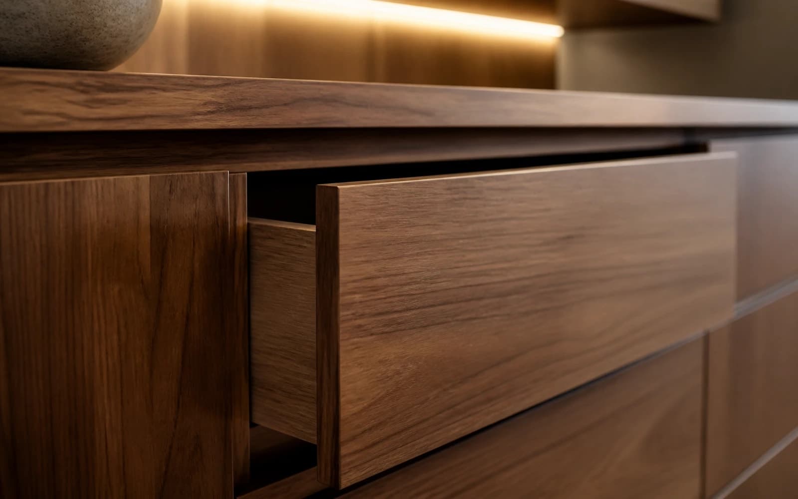 Close-up of warm walnut timber cabinetry with straight grain and a soft-close drawer reveal