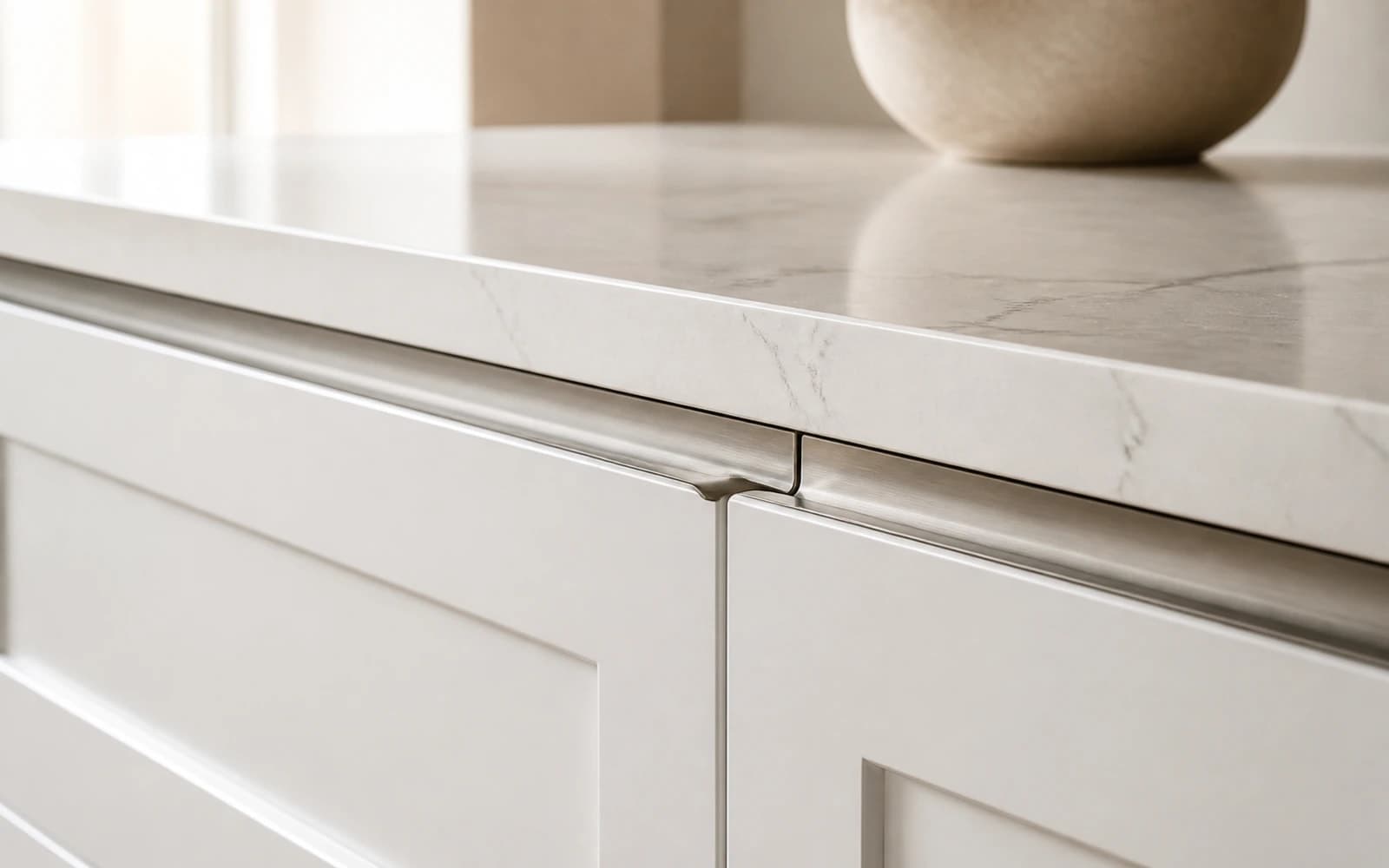 Detail of handleless white shaker cabinetry with a flush stone benchtop and brushed-nickel edge pull